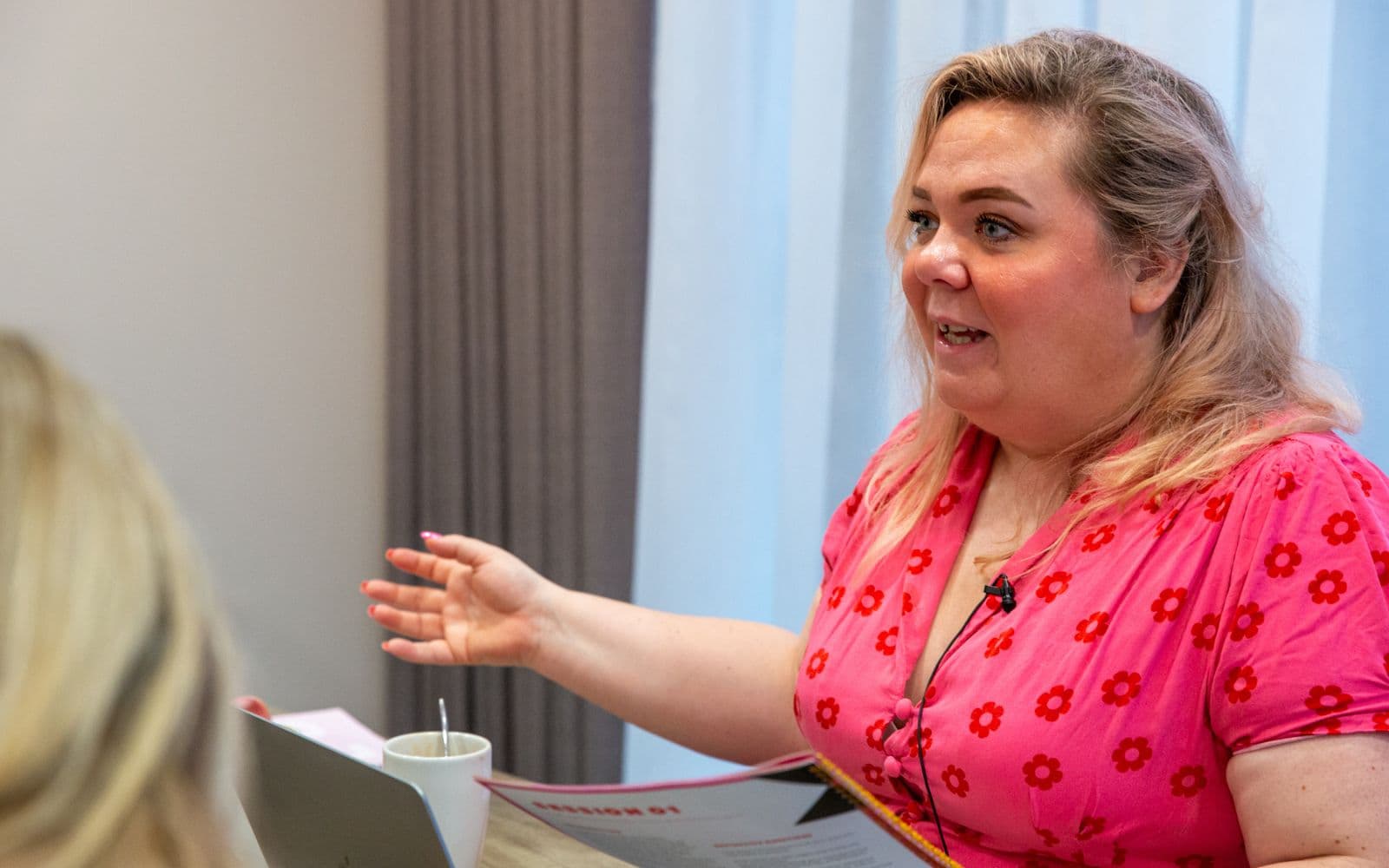 Zoë Dew mid-conversation, gesturing as she talks to someone across a table